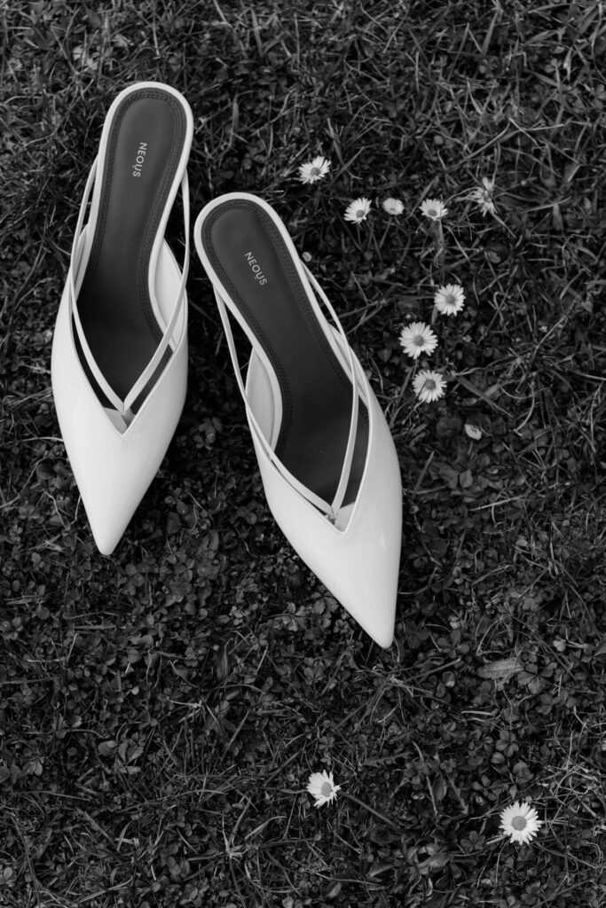 Elegant white heels on grass with daisies, capturing timeless bridal aesthetics