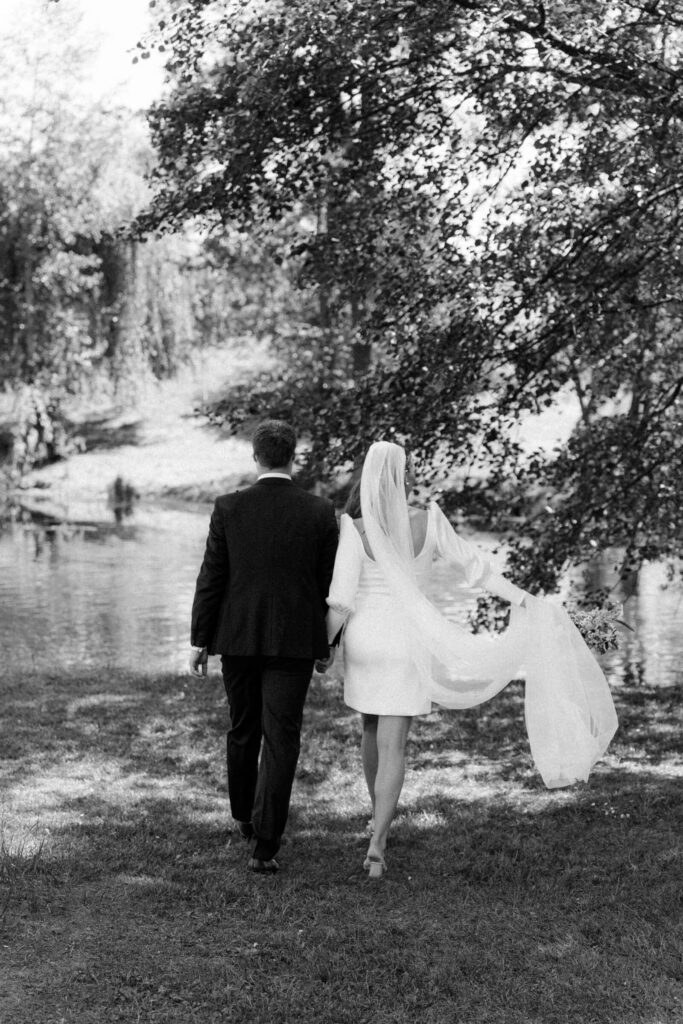 Timeless black and white photo of bride and groom walking by the water in elegant scenery
